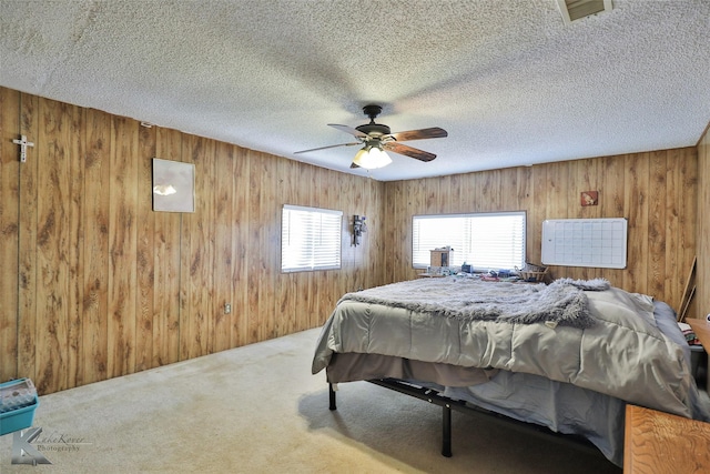 carpeted bedroom featuring a textured ceiling, ceiling fan, and wood walls