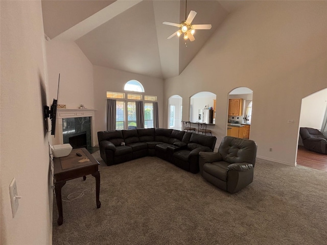 living room with ceiling fan, a premium fireplace, high vaulted ceiling, and carpet