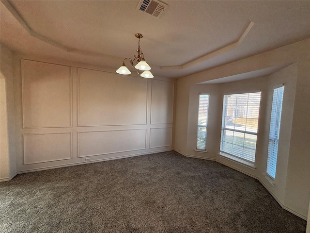 carpeted empty room featuring an inviting chandelier and a tray ceiling