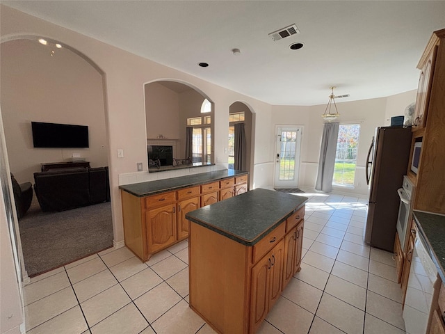 kitchen featuring light tile patterned floors, stainless steel fridge, a center island, decorative light fixtures, and oven