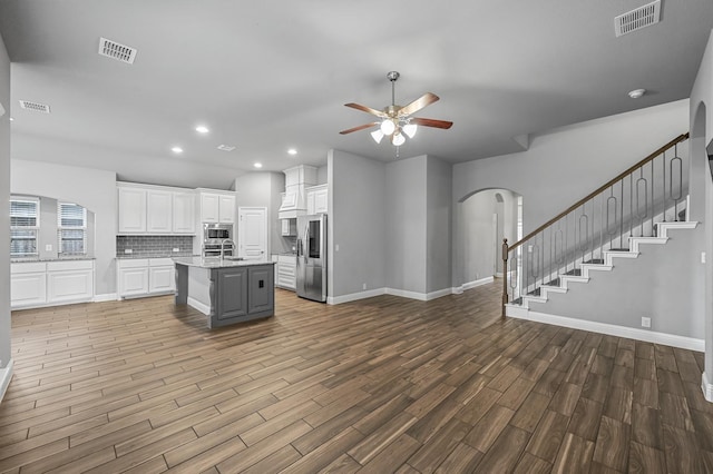 kitchen featuring stainless steel appliances, ceiling fan, hardwood / wood-style flooring, white cabinets, and an island with sink