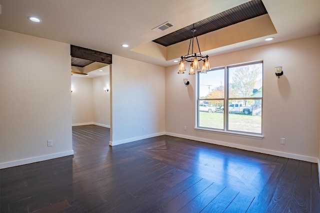 unfurnished room with a tray ceiling, dark hardwood / wood-style flooring, and an inviting chandelier