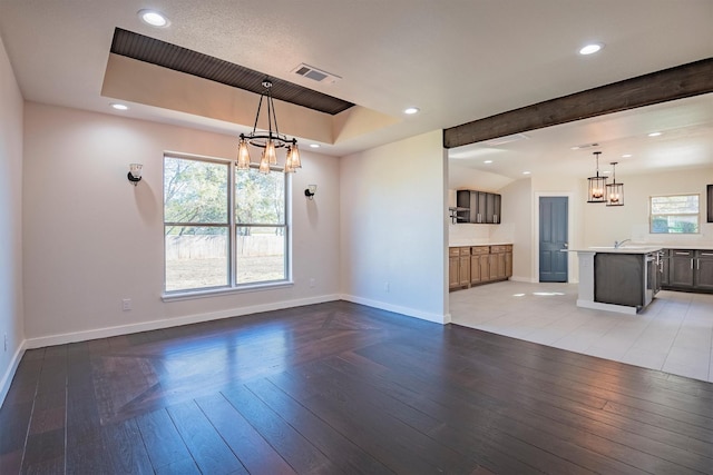 unfurnished living room featuring beamed ceiling, a chandelier, light hardwood / wood-style flooring, and sink