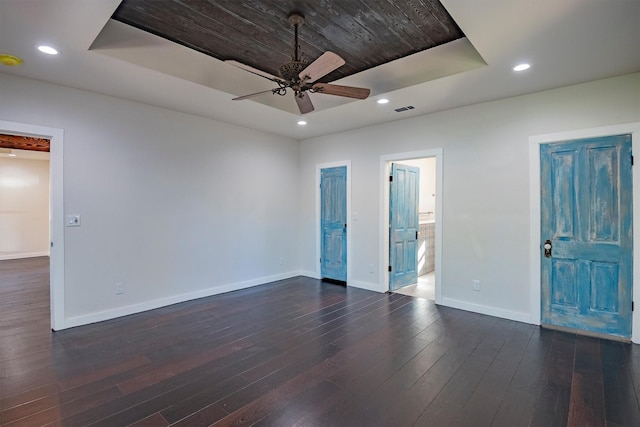 empty room with dark hardwood / wood-style flooring, a tray ceiling, and ceiling fan