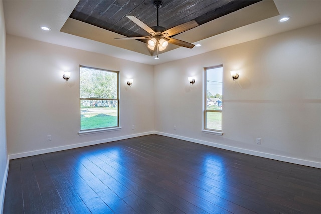 unfurnished room featuring dark hardwood / wood-style floors, ceiling fan, and a tray ceiling