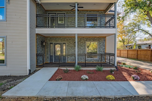 view of exterior entry featuring covered porch, a balcony, and ceiling fan