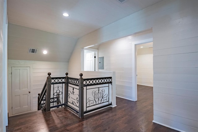 hallway with vaulted ceiling, dark hardwood / wood-style floors, electric panel, and wooden walls