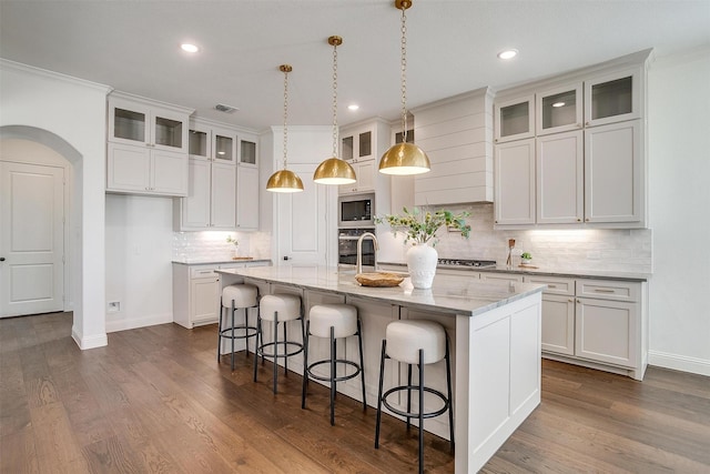 kitchen with appliances with stainless steel finishes, white cabinetry, light stone counters, and a kitchen island with sink