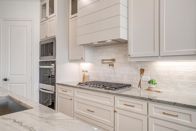 kitchen with decorative backsplash, light stone countertops, white cabinetry, and appliances with stainless steel finishes