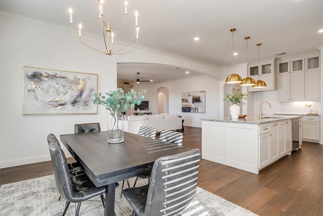 dining room with sink, dark wood-type flooring, ceiling fan with notable chandelier, and ornamental molding