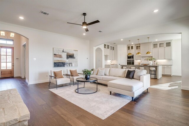 living room with dark wood-type flooring, ornamental molding, sink, and ceiling fan with notable chandelier