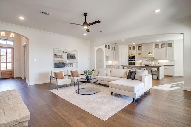 living room with arched walkways, ornamental molding, dark wood finished floors, and baseboards