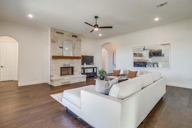 living room with dark hardwood / wood-style floors, ceiling fan, a stone fireplace, and crown molding