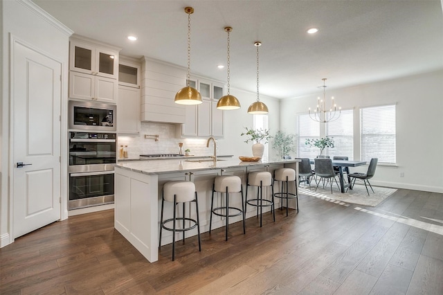 kitchen featuring white cabinetry, dark hardwood / wood-style floors, an island with sink, pendant lighting, and appliances with stainless steel finishes