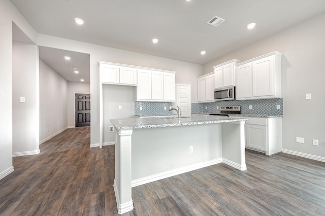 kitchen with white cabinetry, tasteful backsplash, dark hardwood / wood-style floors, a center island with sink, and appliances with stainless steel finishes