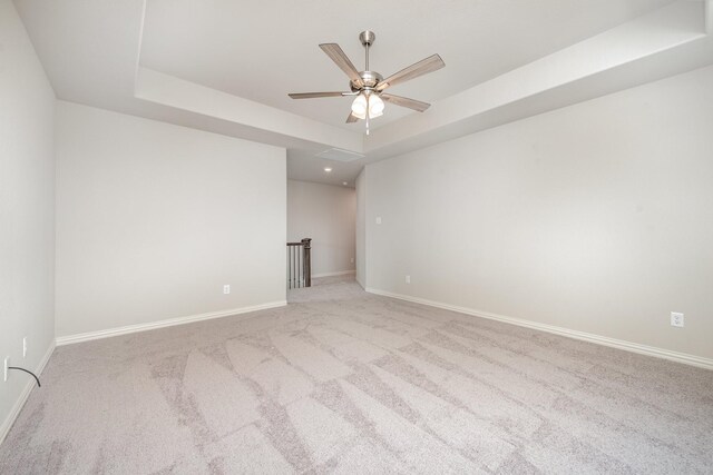 empty room with light colored carpet, ceiling fan, and a tray ceiling