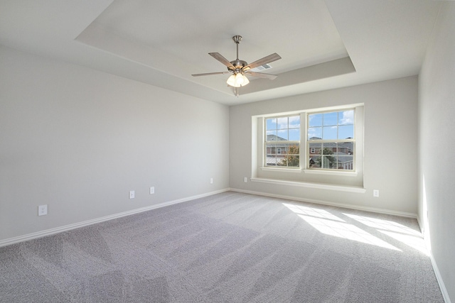 carpeted spare room with a raised ceiling and ceiling fan