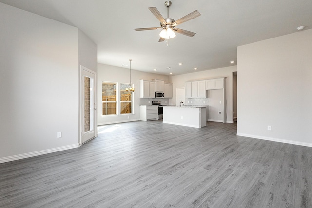 unfurnished living room featuring hardwood / wood-style floors and ceiling fan with notable chandelier