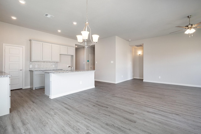 kitchen with backsplash, white cabinets, hanging light fixtures, light wood-type flooring, and an island with sink