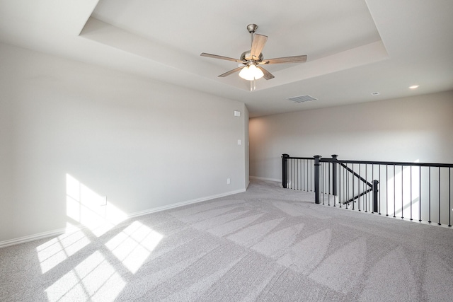 carpeted empty room with a raised ceiling and ceiling fan