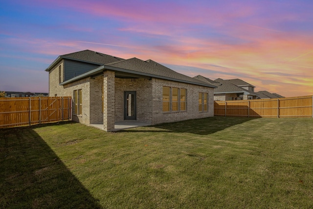 back house at dusk with a patio area and a yard