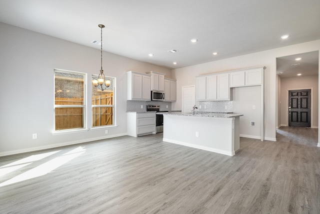 kitchen with light stone countertops, appliances with stainless steel finishes, light hardwood / wood-style floors, and white cabinetry