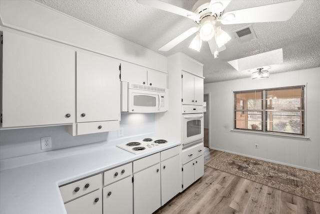 kitchen featuring white cabinetry, a skylight, a textured ceiling, white appliances, and light hardwood / wood-style floors