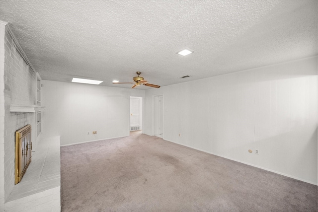 unfurnished living room with ceiling fan, a skylight, a textured ceiling, a brick fireplace, and light colored carpet