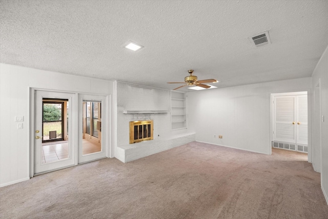 unfurnished living room with built in shelves, a fireplace, light carpet, and a textured ceiling