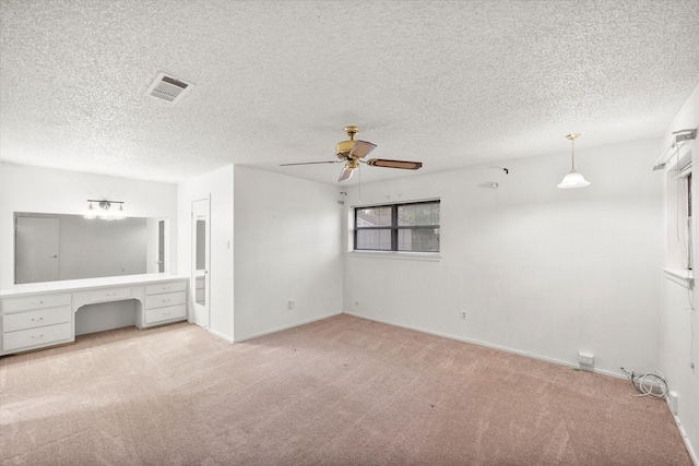 unfurnished living room featuring ceiling fan, light colored carpet, built in desk, and a textured ceiling