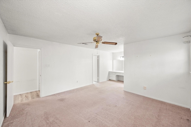 unfurnished room featuring light carpet, a textured ceiling, built in desk, and ceiling fan