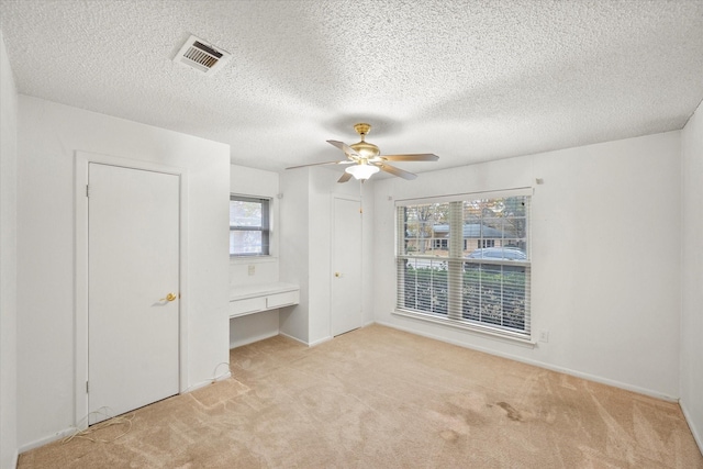 unfurnished bedroom with ceiling fan, built in desk, light carpet, and a textured ceiling