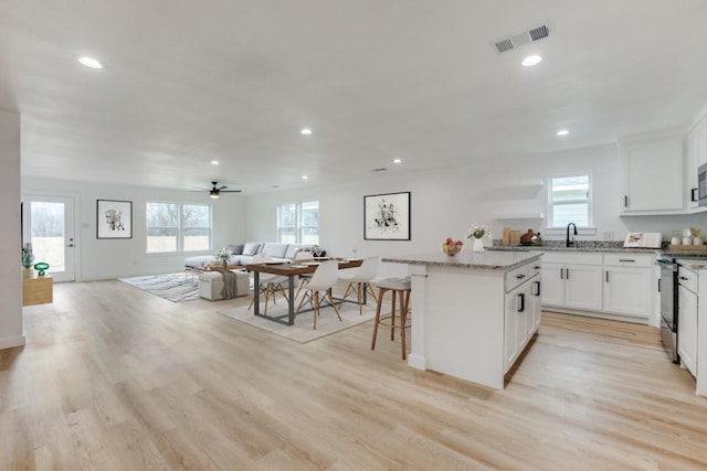 kitchen with stainless steel range with electric cooktop, a center island, a kitchen breakfast bar, light stone countertops, and white cabinets