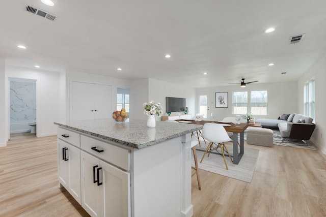 kitchen with a center island, ceiling fan, light stone countertops, light hardwood / wood-style floors, and white cabinetry