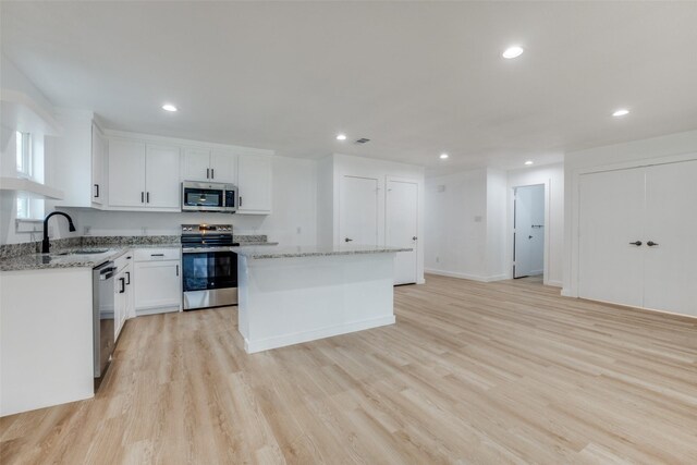 kitchen with sink, white cabinetry, stainless steel appliances, a center island, and light stone counters