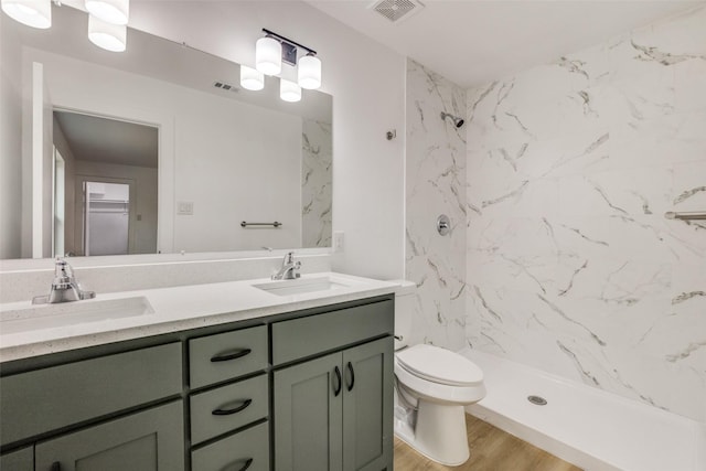 bathroom featuring hardwood / wood-style flooring, tiled shower, vanity, and toilet