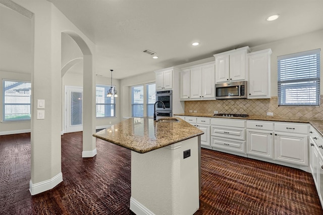 kitchen featuring light stone counters, white cabinetry, hanging light fixtures, an island with sink, and stainless steel appliances