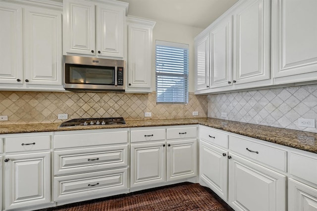 kitchen with white cabinetry, appliances with stainless steel finishes, backsplash, and dark stone countertops