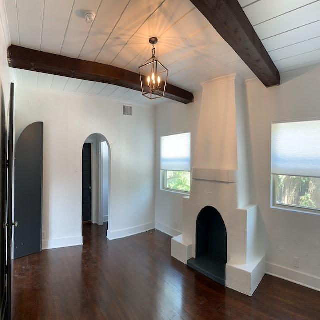 unfurnished living room featuring lofted ceiling with beams, dark wood-type flooring, and a notable chandelier