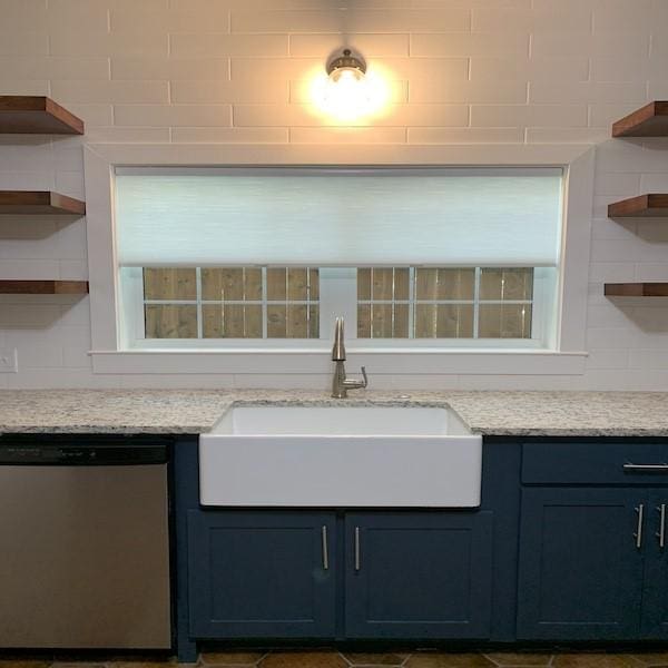 interior space with light stone counters, blue cabinets, dishwasher, and sink