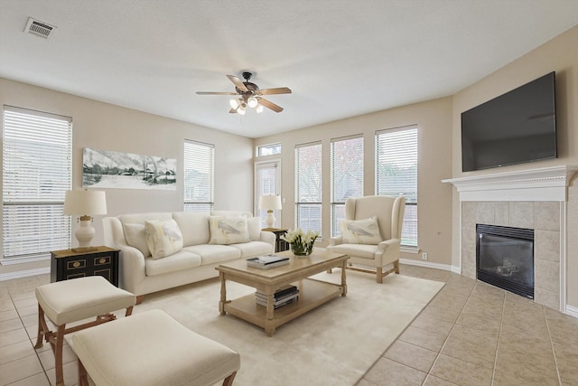 living room with ceiling fan, light tile patterned flooring, a textured ceiling, and a tiled fireplace