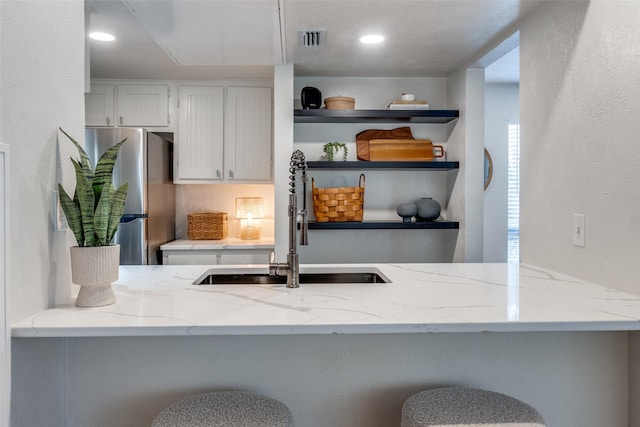 kitchen with sink, light stone countertops, white cabinetry, kitchen peninsula, and stainless steel refrigerator