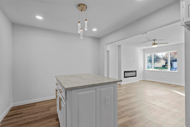 kitchen featuring ceiling fan, wood-type flooring, white cabinets, a center island, and hanging light fixtures