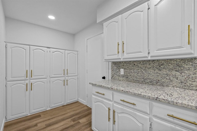 kitchen featuring backsplash, white cabinetry, light stone countertops, and hardwood / wood-style flooring