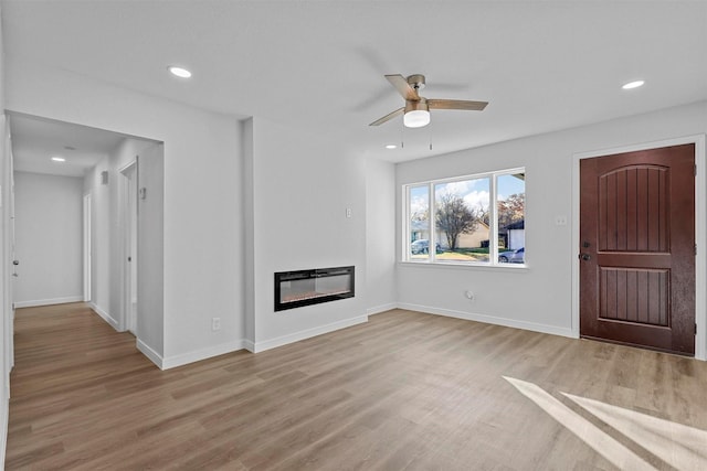 unfurnished living room featuring baseboards, a glass covered fireplace, light wood-style flooring, and heating unit