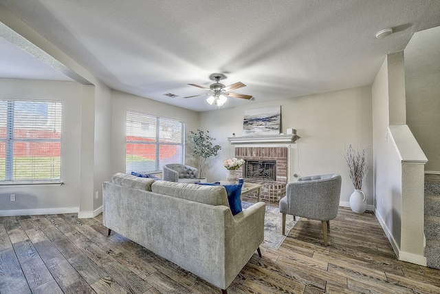 living room featuring ceiling fan, dark wood-type flooring, a textured ceiling, and a fireplace