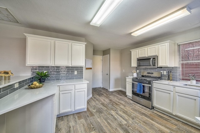 kitchen with wood-type flooring, appliances with stainless steel finishes, white cabinets, and decorative backsplash