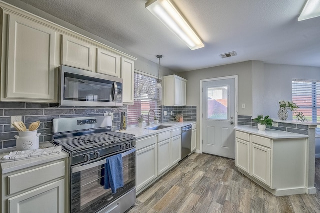 kitchen with sink, appliances with stainless steel finishes, hanging light fixtures, dark hardwood / wood-style flooring, and kitchen peninsula