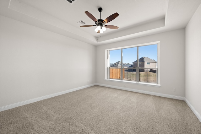 carpeted empty room featuring visible vents, baseboards, ceiling fan, and a tray ceiling
