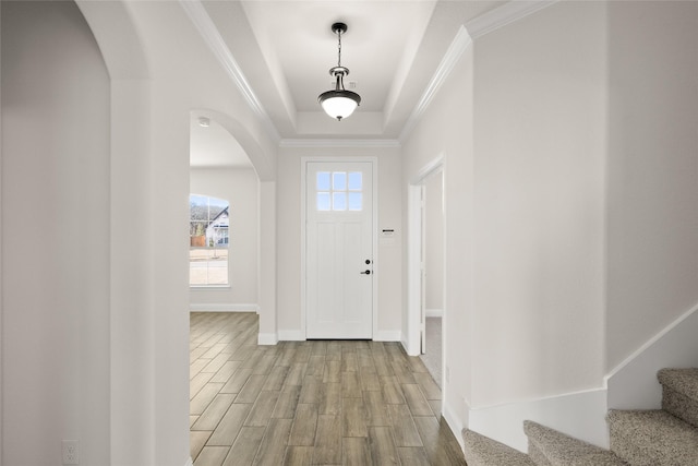 foyer featuring light wood-type flooring, crown molding, and a raised ceiling